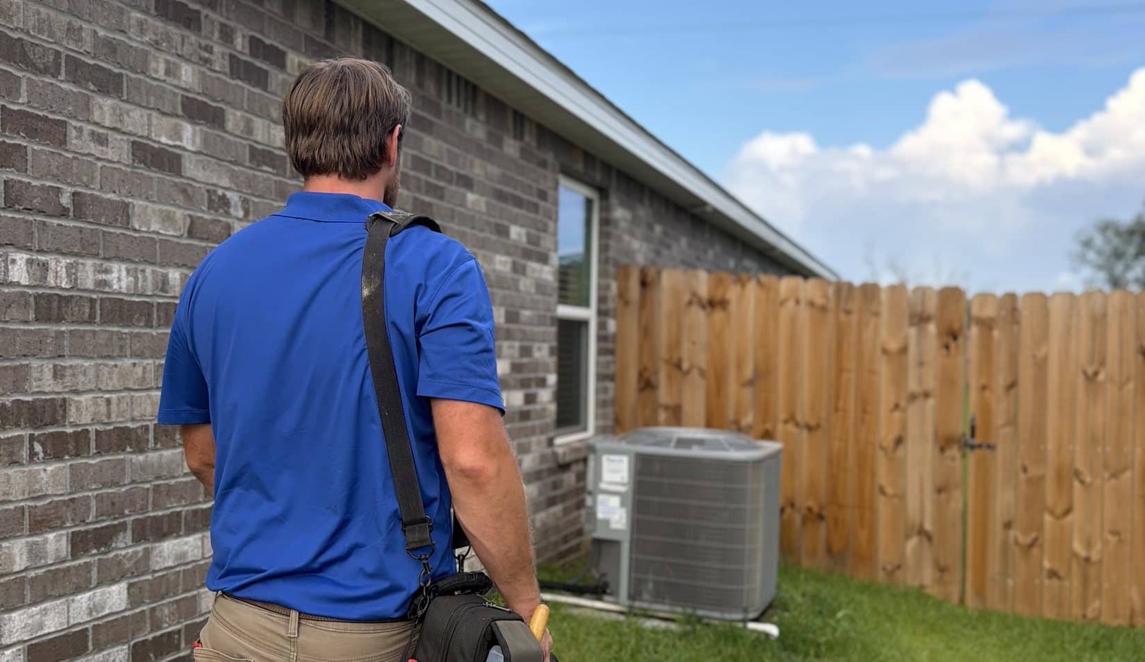 ACExperts technician walking to a residential outdoor unit beside a brick home in Baldwin County
